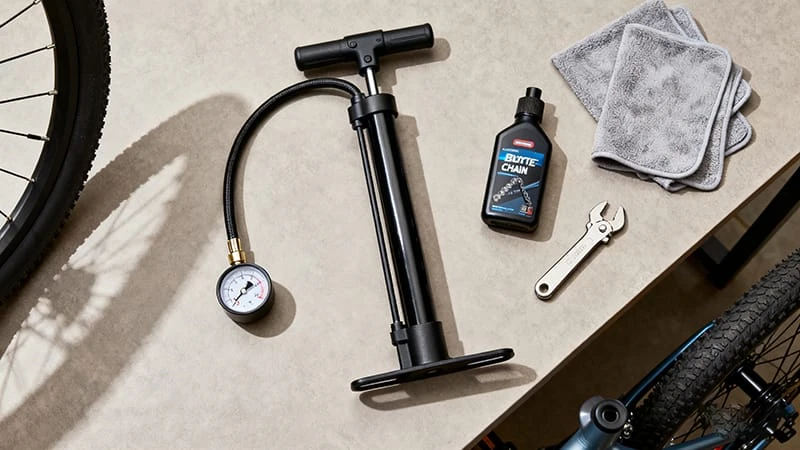 A flat lay of essential electric bicycle maintenance tools including a pump, lube, hex wrenches, and rags.